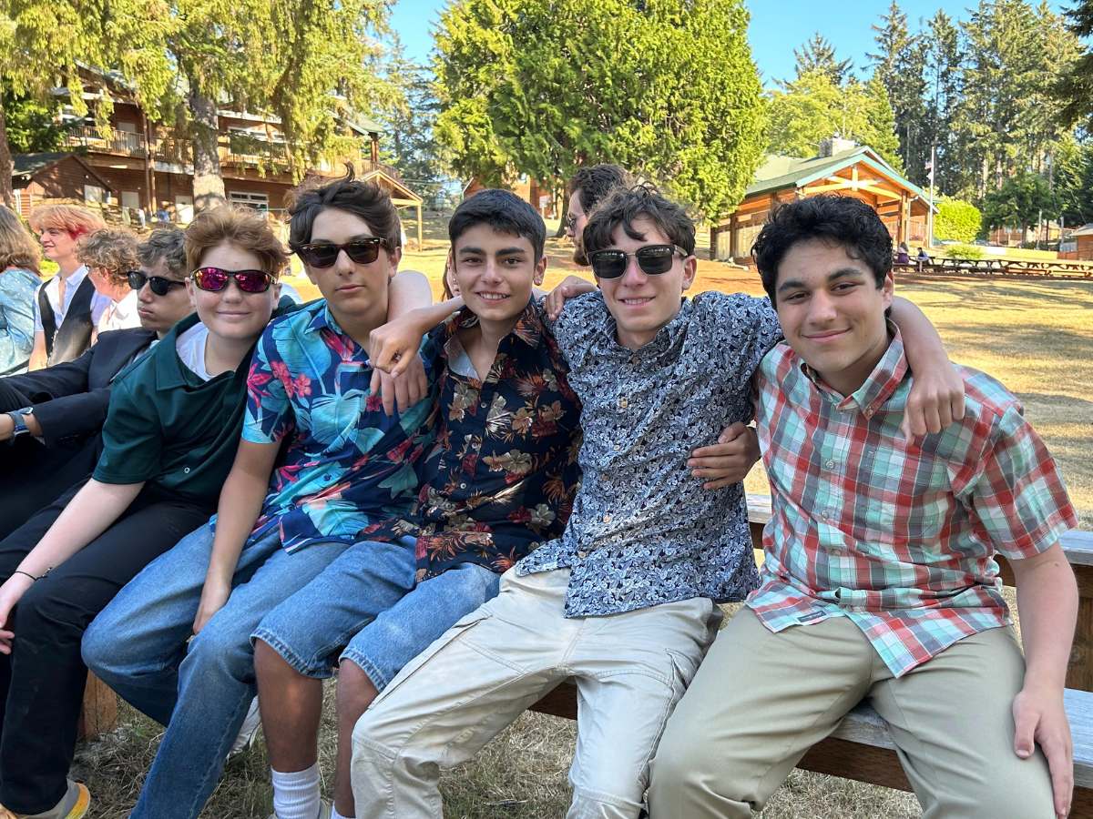 A group of male campers sitting on a bench with arms around each other