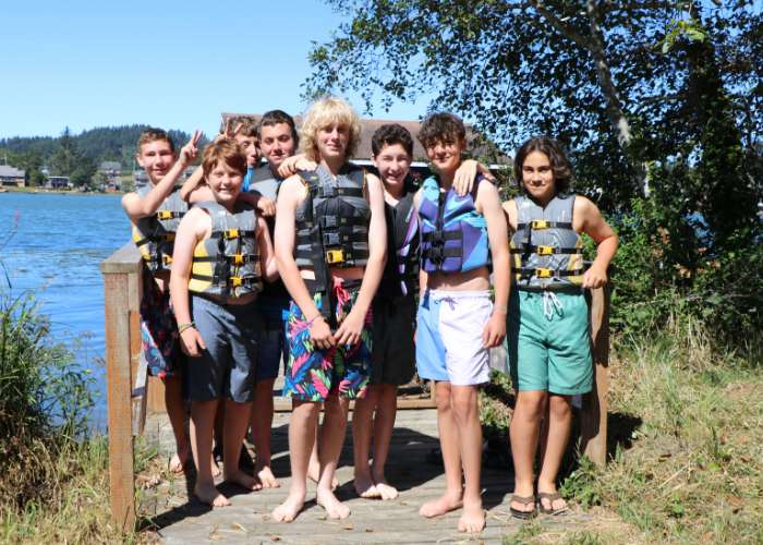 A group of male campers standing by the lake wearing lifevests
