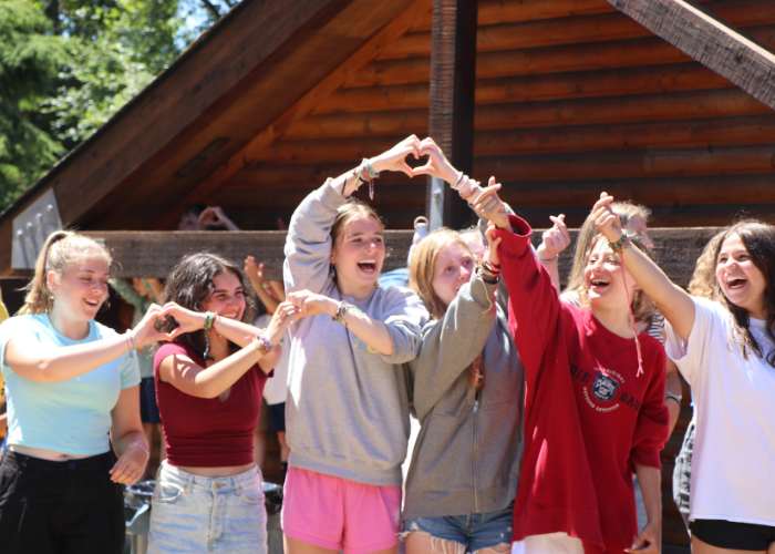 A group of female campers making heart shapes with their fingers together