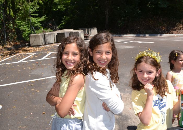 two campers standing back to back smiling to the camper and another camper standing besides them holding her chin and smiling