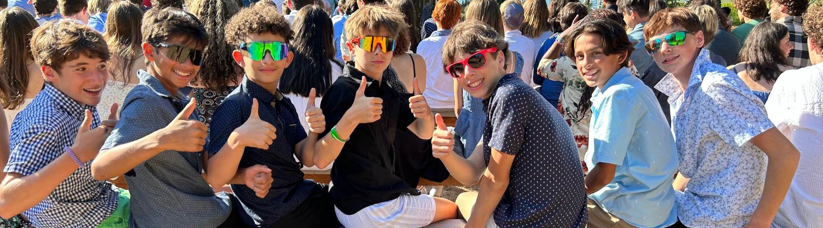teenagers sitting on a bench wearing sunglasses holding up their thumbs in two thumbs up